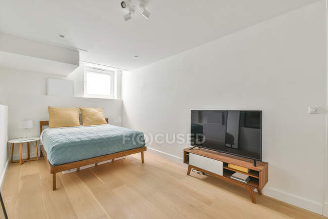 Intérieur moderne de petite chambre avec lit confortable et TV sur armoire en bois dans chalet — Photo de stock