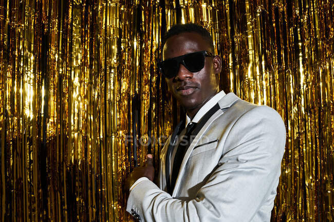 Cool African American male in jacket and tie posing against tinsel while celebrating New Years Eve — Stock Photo