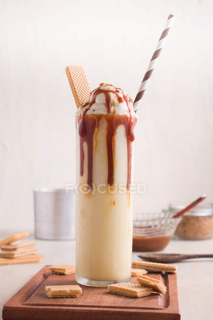 Glass with sweet caramel milkshake with vanilla ice cream and wafer cookies served on table — Stock Photo