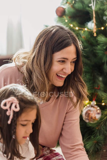 Cheerful mom with girl against decorated fir tree during New Year holiday in house room — Stock Photo
