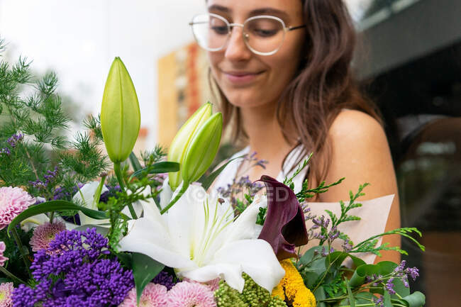 Обрізати чарівну молоду жінку в окулярах з квітучим квітковим букетом проти скляної стіни в місті вдень — стокове фото