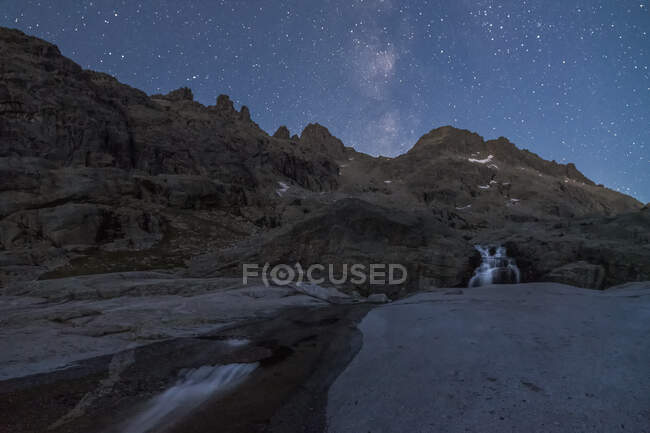 Вражаючі краєвиди грубих скелястих утворень з водоспадом, що впадає в озеро під безхмарним зоряним небом вночі. — стокове фото