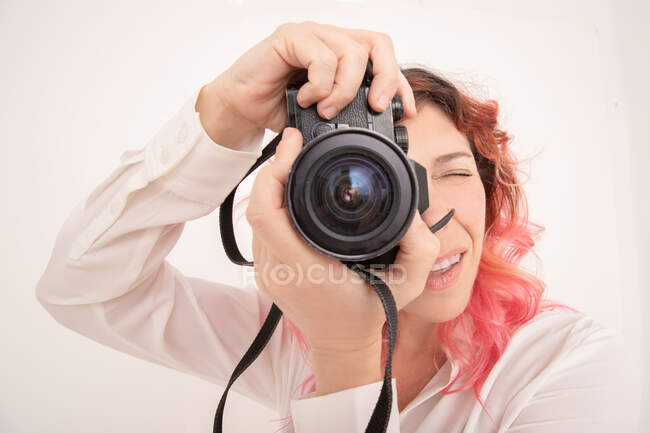 Fotógrafo feminino pensativo com cabelo rosa tirando foto na câmera fotográfica profissional na sala de luz — Fotografia de Stock