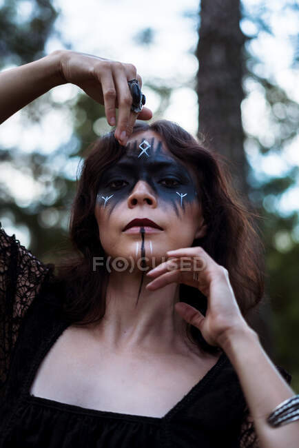 Headshot de bruxa mística com rosto pintado dançando com braços em bosques sombrios e olhando para a câmera — Fotografia de Stock
