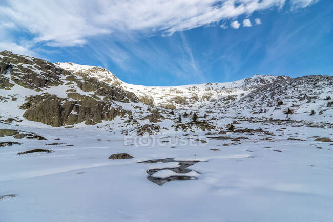 Pintoresco paisaje de ásperas montañas rocosas cubiertas de nieve ubicadas en el campo bajo el cielo azul nublado a la luz del día - foto de stock