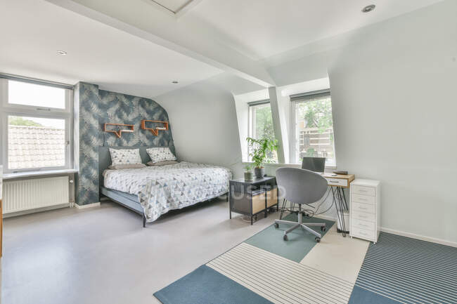 Cama macia com roupa de cama branca colocada perto do local de trabalho com laptop aberto em espaçoso quarto leve no apartamento — Fotografia de Stock