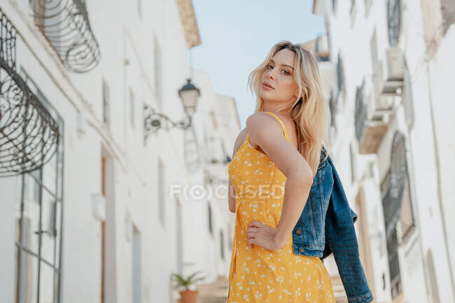 Seitenansicht einer jungen Frau im Sommer-Outfit, die zwischen alten Gebäuden in einer Gasse steht — Stockfoto