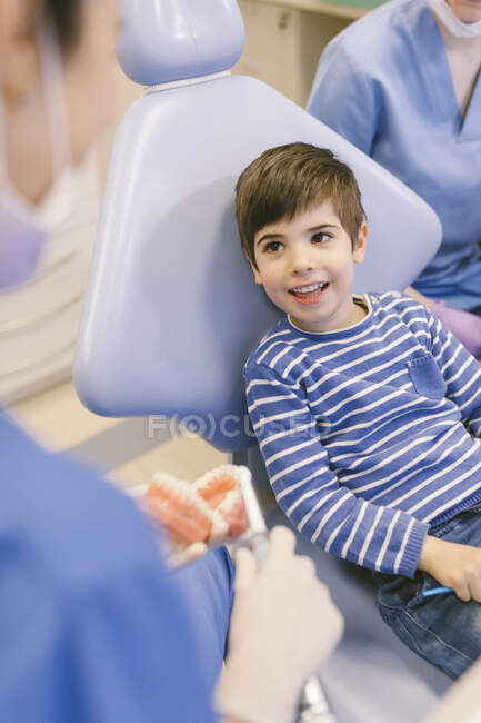 Усміхнена жінка-ортодонта навчає пацієнта зубною щіткою чистити зуби на моделі щелепи в стоматологічній клініці — стокове фото