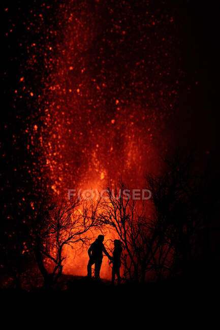 Silhouette eines Paares gegen explodierende Lava und Magma, die aus dem Krater strömen. Cumbre Vieja Vulkanausbruch auf La Palma Kanarische Inseln, Spanien 2021 — Stockfoto