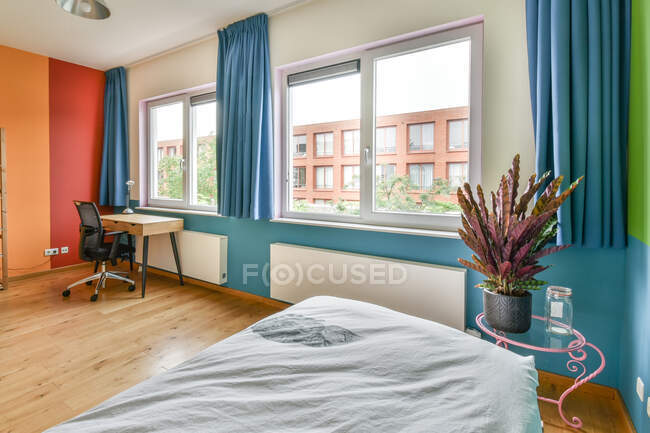 Contemporary bright bedroom interior decorated with potted plant with chair and table near window with blue curtains — Stock Photo
