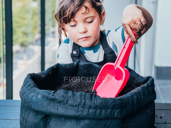 Девочка играет с пластиковой лопатой в кастрюле с почвой для растений — стоковое фото