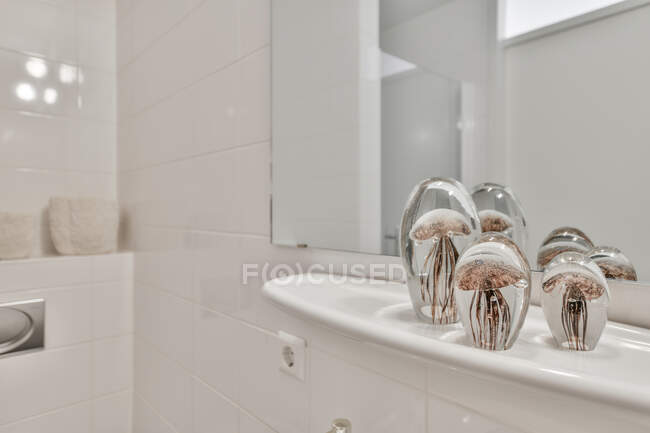 Dekorative Glasquallen auf weißem Regal gegen Spiegel im hellen, geräumigen Badezimmer platziert — Stockfoto