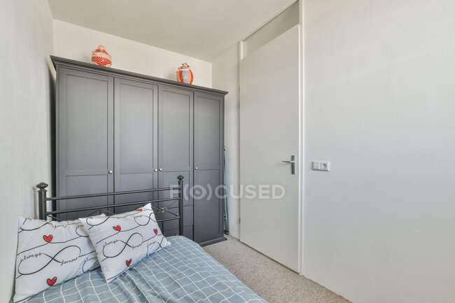 Интерьер небольшой спальни с металлической кроватью под одеялом и большой шкаф рядом с дверью — стоковое фото