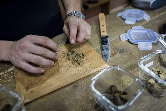 Cultivez des bourgeons de fleurs de marijuana séchées en lambeaux mâles anonymes sur une planche à découper contre un couteau dans la chambre — Photo de stock