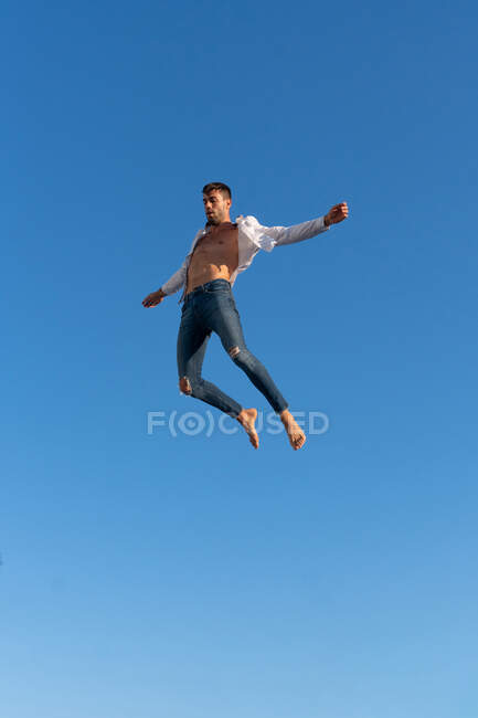 Снизу вид энергичного спортсмена в модной одежде, выступающего в голубом небе при солнечном свете — стоковое фото