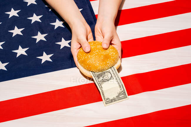 From above of crop unrecognizable person with bun halves and dollar bill over national American flag on Independence Day — Stock Photo