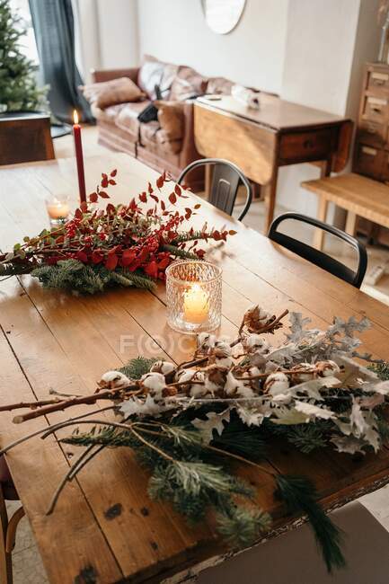 De cima de buquê de Natal festivo com ramos de algodão, abeto e ramos de eucalipto e ramos vermelhos brilhantes com bagas colocadas na mesa de madeira com velas no quarto — Fotografia de Stock