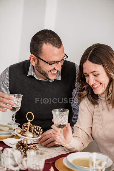 Cultivo alegre pareja con vasos de bebida alcohólica interactuando mientras se ríe en la mesa con sopas de crema durante las vacaciones de Año Nuevo - foto de stock