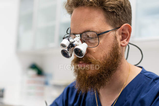 Cirujano veterinario con barba no arreglada operando con lupas encima de sus gafas - foto de stock