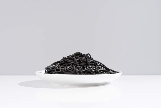 Estudio minimalista con espaguetis de tinta de calamar negro en cuenco cerámico completo sobre mesa blanca - foto de stock