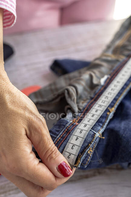 Angle élevé de la couturière femelle anonyme de culture mesurant la taille du jean sur une table en bois le jour — Photo de stock