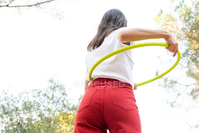 Знизу ззаду видно невпізнаваних жінок-підлітків у червоних джинсах, які тримають обруч, при цьому проводячи вільний час у парку — стокове фото