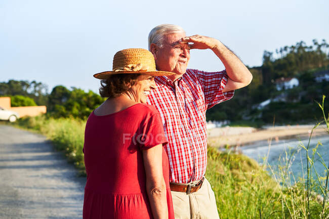Pareja de ancianos de pie uno junto al otro y disfrutando de la vista del mar en un día soleado - foto de stock