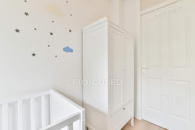 Маленьке дерев'яне дитяче ліжечко, розміщене біля шафи в спальні з мінімалістичним інтер'єром вдень — стокове фото