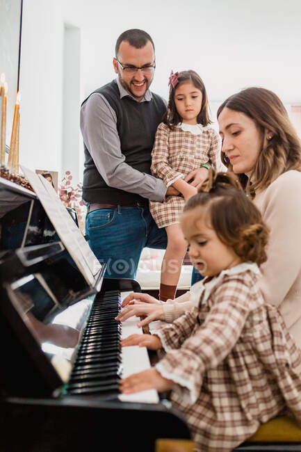 Чарівна дитина з мамою грає на піаніно проти усміхненого батька, що обіймає дочку в кімнаті — стокове фото