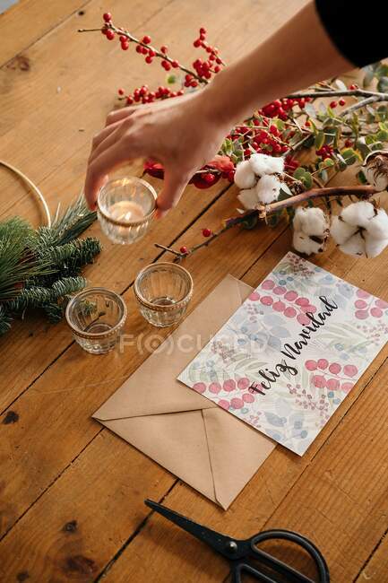 From above of crop unrecognizable person putting burning candle on wooden table with postcard and decorative bouquet — Stock Photo