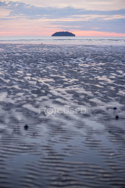 Sandy shore washed by shallow water of sea with hill on horizon under sunset sky in Malaysia — Stock Photo