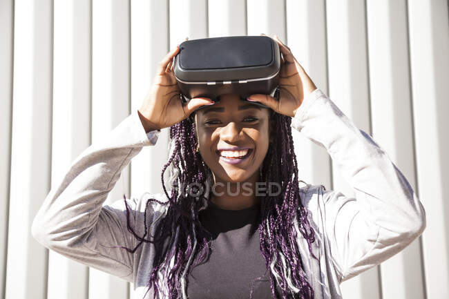 Aufgeregte junge Afroamerikanerin in VR-Headset unterhaltsam und spielt virtuelles Spiel gegen grau gestreifte Wand — Stockfoto
