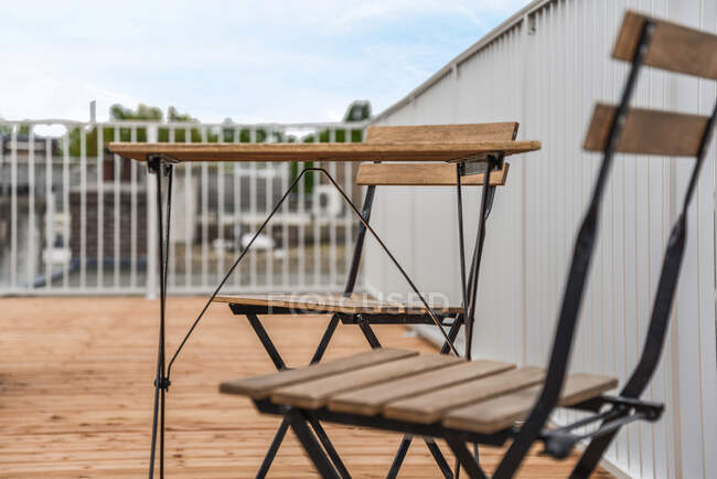 Sillas colocadas cerca de la mesa de madera en el balcón vallado del distrito residencial de los suburbios durante el día - foto de stock