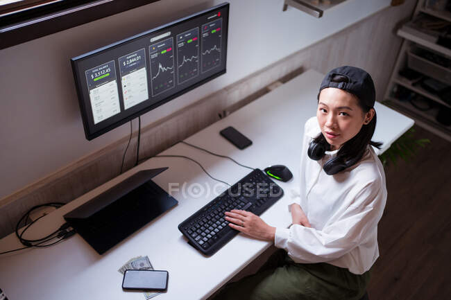 High angle concentrated Asian female working on computer with charts showing dynamic of changes in value of cryptocurrency at convenient workplace — Stock Photo
