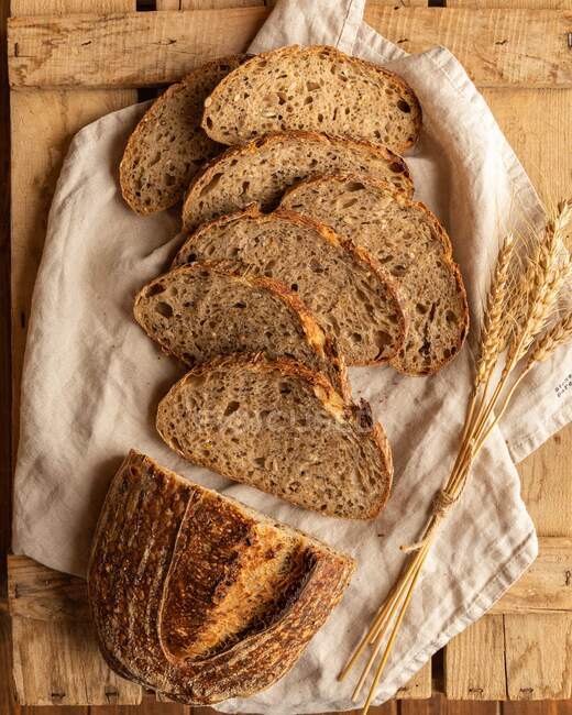 Вид сверху свежих кусочков хлеба с пшеничными пряностями на складной ткани на деревянной поверхности — стоковое фото