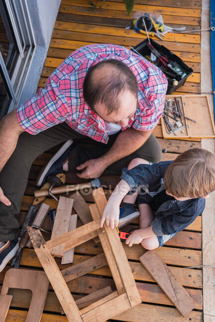 Зверху незахищений зрілий тато з уважним хлопчиком вимірює дерев'яні блоки стрічкою, проводячи час на розмитому фоні — стокове фото