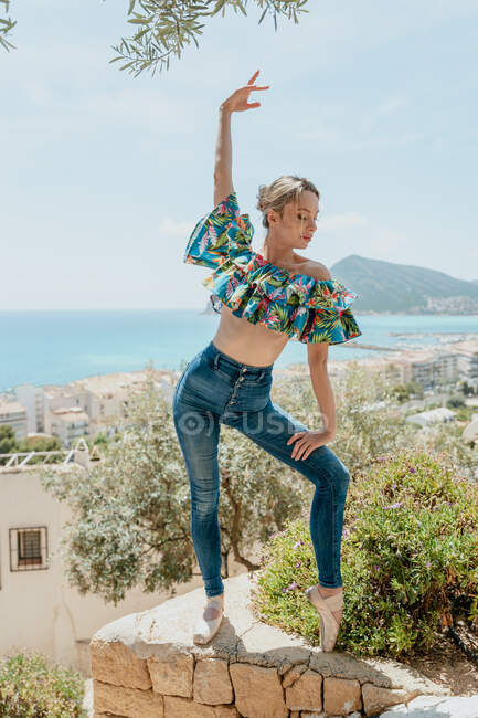 Junge Ballerina steht in Spitzenschuhen auf Zehenspitzen und hebt den Arm in der alten Küstenstadt — Stockfoto