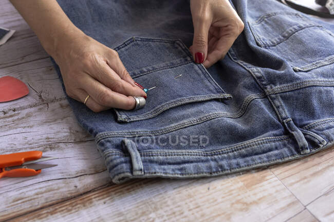 From above of crop woman sewer attaching pin to jeans on wooden table in daytime — Stock Photo