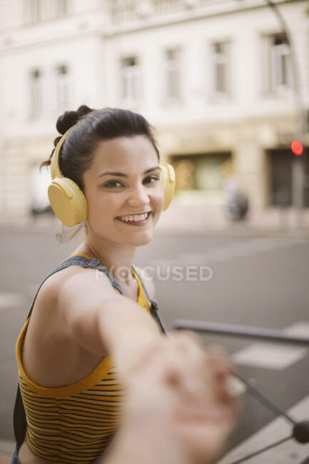 Side view of positive young female listening to music in wireless headphones and holding hand while looking at camera — Stock Photo