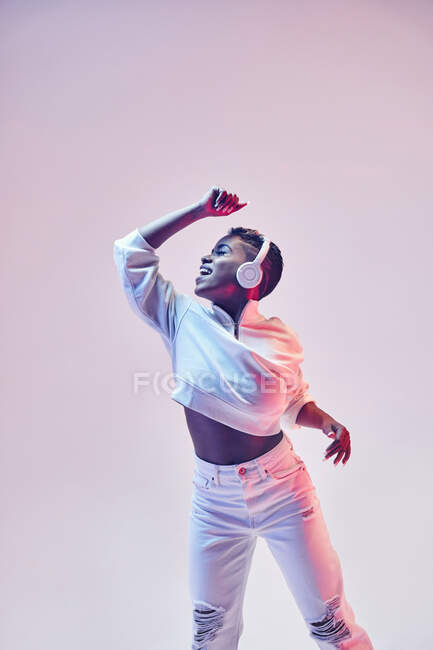 Femme ethnique énergique dans des écouteurs sans fil et vêtements à la mode dansant hip hop avec bouche ouverte — Photo de stock