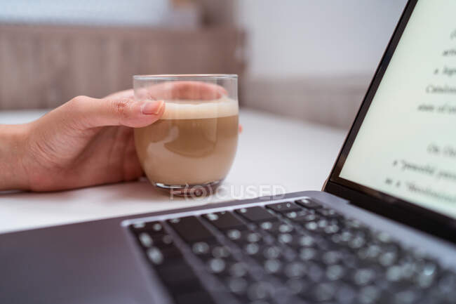 Обрезанная неузнаваемая женщина-блоггер за столом с нетбуком и кофе — стоковое фото
