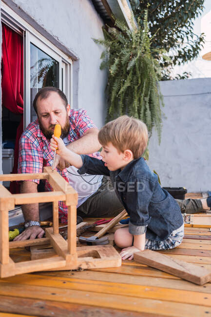 Reifer Vater erklärt Sohn, wie man Schrauben in Holzklötze einschraubt, während man auf der Promenade sitzt — Stockfoto