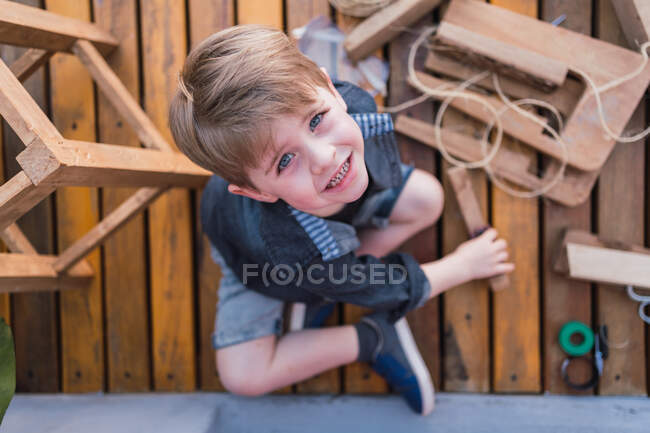 Top view of child with blue eyes and crossed legs looking at camera between wooden blocks — Stock Photo