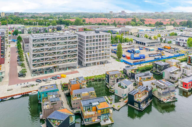 Drohnen-Ansicht zeitgenössischer Häuserfassaden gegen Seebrücke und Hausboote auf dem plätschernden Fluss in Amsterdam Niederlande — Stockfoto