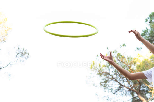 Angolo basso di coltura persona anonima gettando hula hoop in aria divertendosi sotto il cielo bianco nel parco — Foto stock