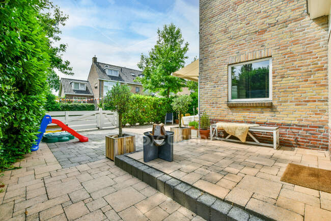 Житловий сад з дитячим майданчиком в цегляному будинку з зеленими рослинами і тротуарами — стокове фото