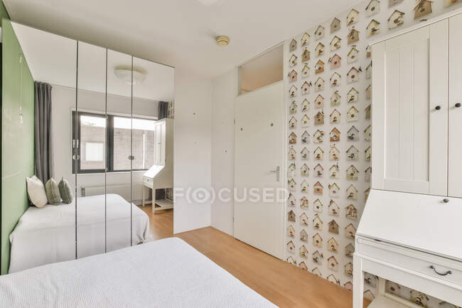 Desk cabinet between wall with house pattern and bed reflecting in mirror closet in daylight — Stock Photo
