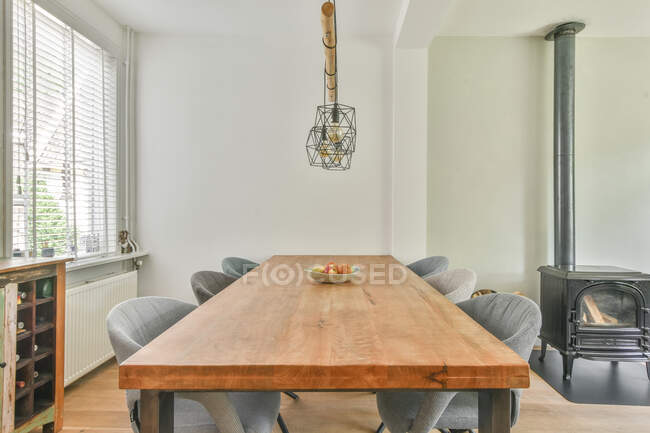 Mesa de madera y cómodas sillas grises colocadas cerca de la chimenea en el comedor en el apartamento durante el día - foto de stock