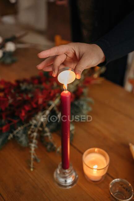 Crop unrecognizable woman lightning candle placed on wooden table with Christmas decorations in room — Stock Photo