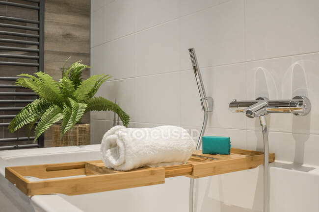 Білий рушник на дерев'яній полиці на ванні, наповненій водою у ванній кімнаті з плиткою стін — стокове фото
